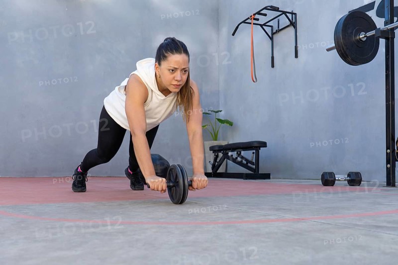 Concentrated sportswoman performing an abdominal exercise using an ab wheel in her home gym, showcasing dedication and strength in her fitness routine