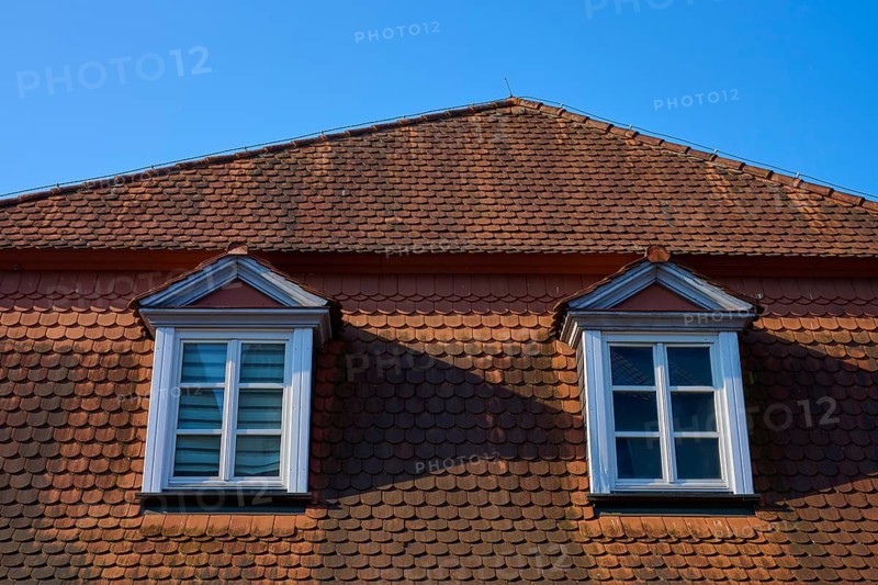Sloping red tiles and dormers with white framed windows under blue sky, Erbach, Odenwald, Hesse, Germany