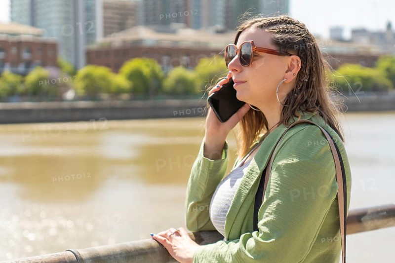 Businesswoman wearing sunglasses talking on smartphone near river in city