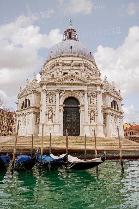 Majestic Venice church with intricate architecture reflects in calm waters. Gondolas line the canal in this breathtaking scene, capturing the essence of Italy's beauty