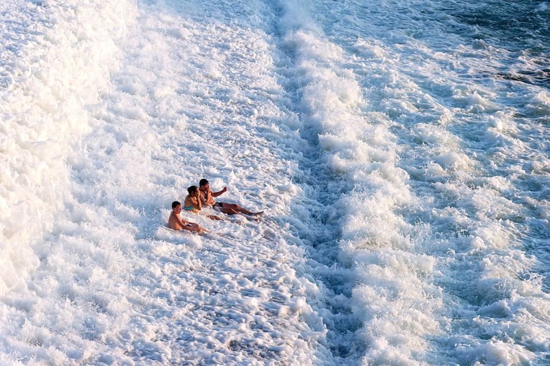 Young people bathing in spray from the Lech weir, sliding down the cascades through white foaming water, river Lech, Landsberg am Lech, Upper Bavaria, Bavaria, Germany