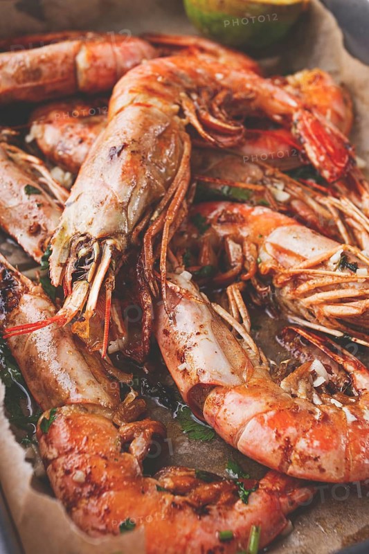 Juicy grilled shrimp, placed on a baking sheet lined with parchment paper, garnished with herbs and lemon