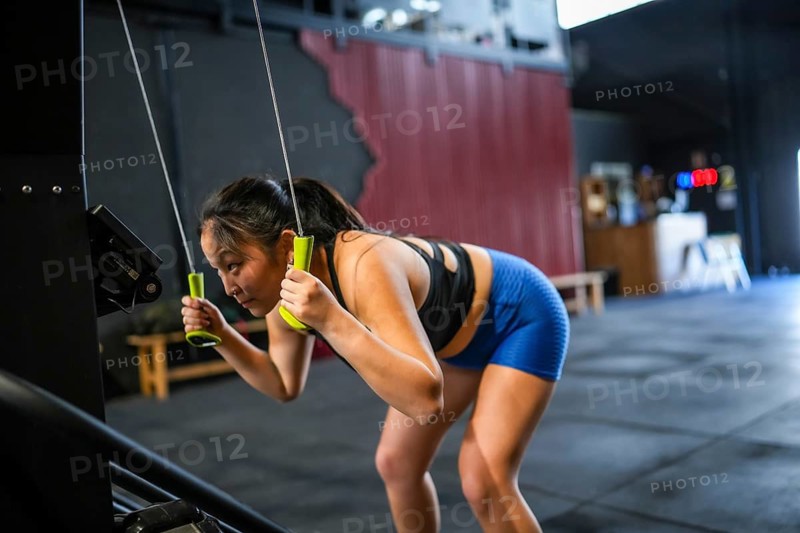 Side view of a Chinese woman exercising using lat machine pulling weights in a cross training gym