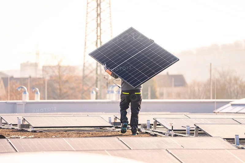 Technician carries a solar panel for installation on a roof in an urban environment, PV assembly at OBI Baumarkt, Mühlacker, Enzkreis, Germany