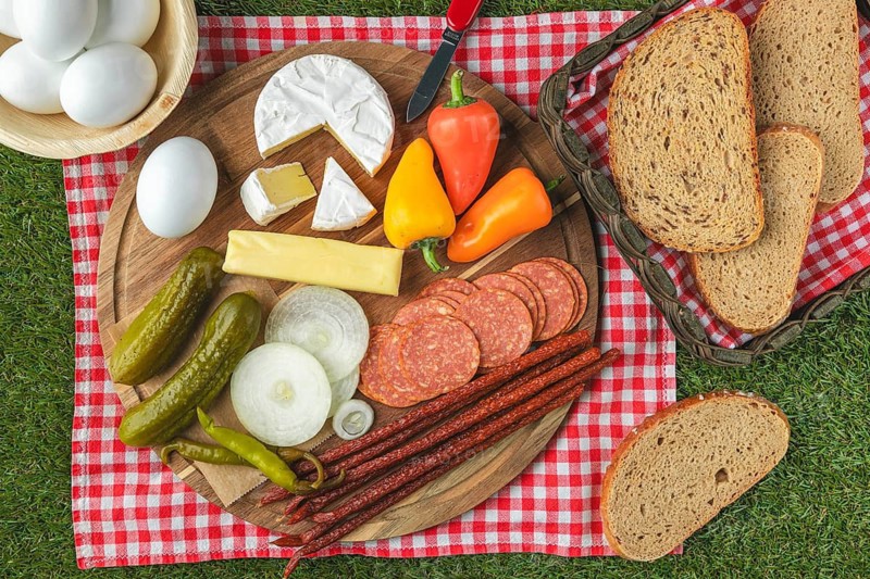 Board snack arranged on picnic blanket, vegan sausage, cheese, bread, eggs and peppers