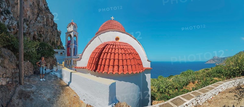 The red-domed church of Panagia Wrisiani is located on a rocky coast overlooking the blue sea under a clear sky, Mesochori, Karpathos, South Aegean, Greece