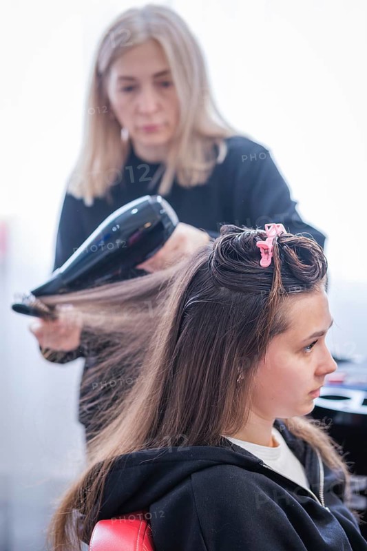 A hair stylist is drying a woman's hair with a blow dryer during a keratin hair treatment at a beauty salon. The stylist focuses on smoothing and straightening the woman's hair