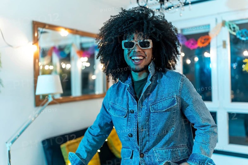 Portrait of a happy young latin man with curly hair and sunglasses smiling in a home night party