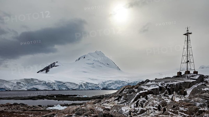 Tower over snow-covered rocks in front of an icy island under a cloudy sky, The coast and landscape of Antarctica