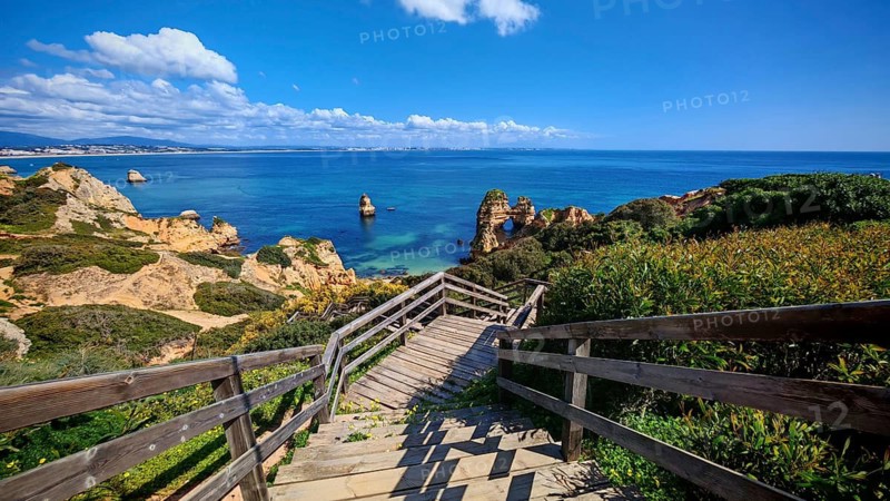 Wooden staircase with breathtaking views of the sea, rock arches and cliffs under clear skies, Praia do Camilo, Lagos, Algarve, Portugal