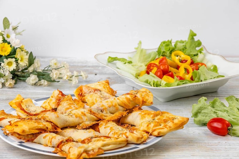 Freshly baked pizza sticks, pizza, colourful salad and flowers in the background