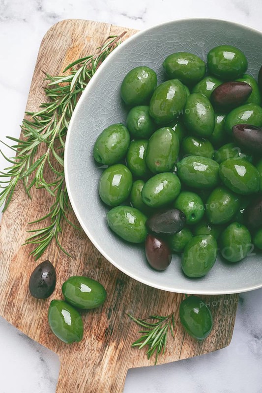Chalkidiki olives, classic Greek green olives, in a bowl on a cutting board, top view, without people