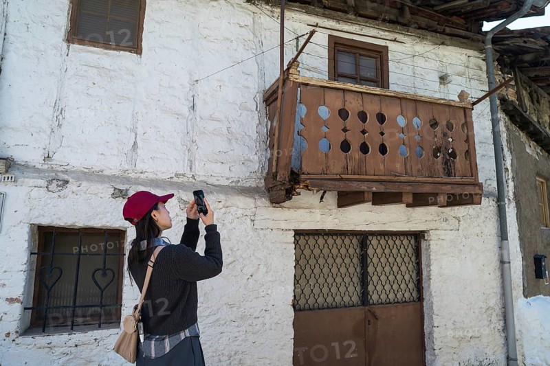 An Asian woman takes a photo of rustic architecture while exploring the charming village of Cuevas del Valle, nestled in the scenic Sierra de Gredos, Avila, Spain