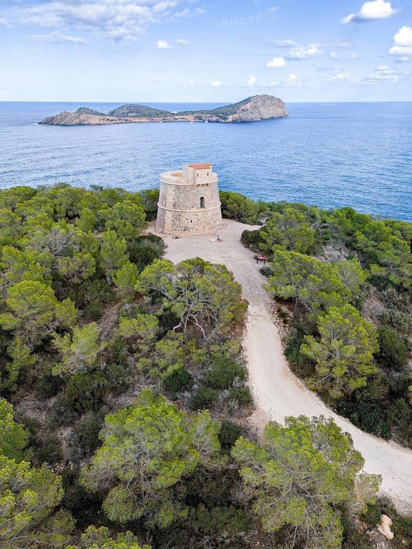 Historic defence defence tower Torre d'en Valls on a tree-covered hill overlooking the sea and the Isla de Tagomago, Ibiza, Balearic Islands, Spain