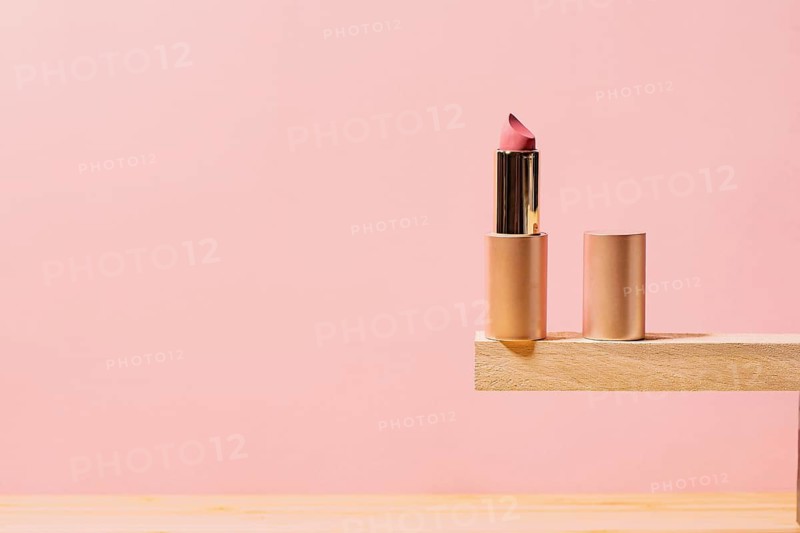 A stylish rose lipstick partially twisted up, placed on a wooden shelf with a pink background, emphasizing modern cosmetic elegance