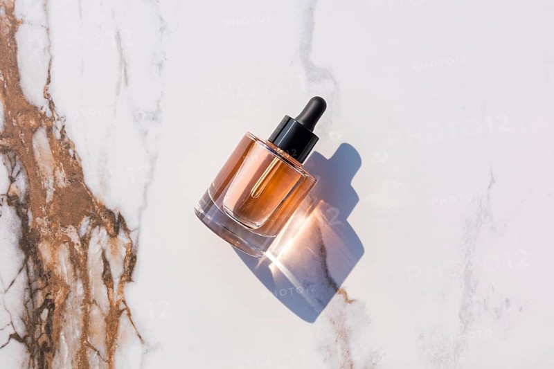 A sleek glass dropper bottle with amber liquid, casting a shadow on a marble surface. Sunlight enhances its elegant appearance, ideal for beauty and skincare concepts