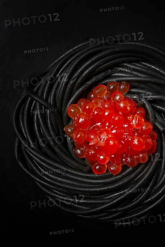 Black spaghetti with red caviar, pasta, on a black background, top view, no people