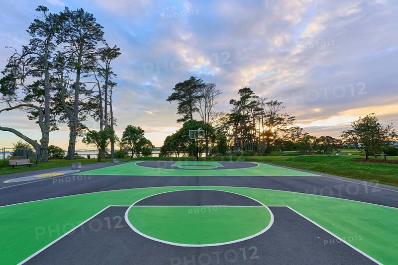 A green basketball court in a natural setting with trees and a dramatic sunrise sky, Coyle Park, Auckland, North Island, New Zealand