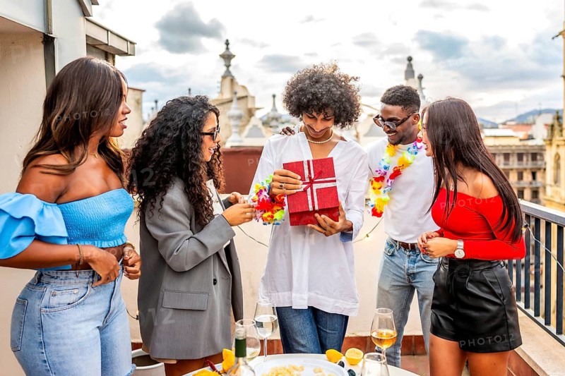 Man receiving a birthday present of his multi-ethnic friends during a rooftop party