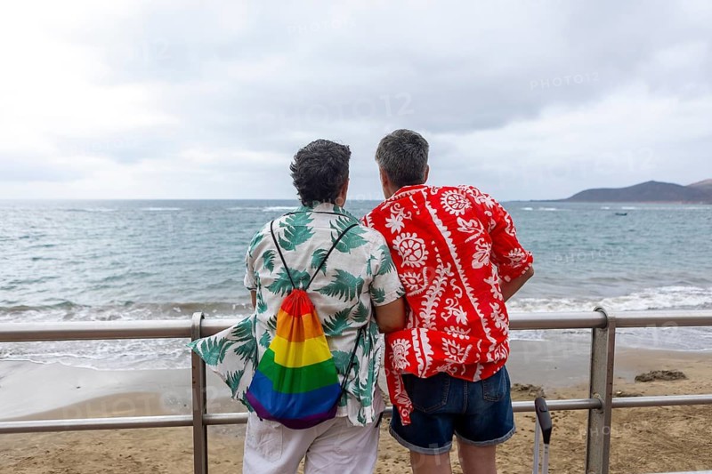 Back view of two unrecognizable women in vibrant summer attire embrace, gazing out at the ocean, during their summer holidays, symbolizing love and togetherness