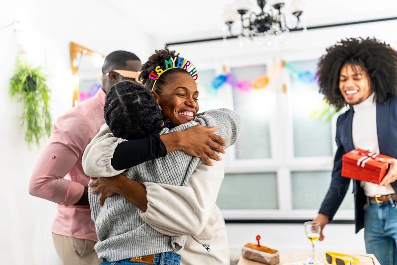 Latin young woman embracing multi-ethnic friends celebrating birthday party at home