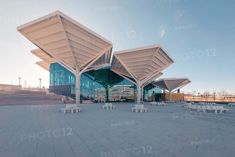 Architectural view of a modern transport interchange located in Valdebebas, Madrid, featuring sweeping canopy designs, expansive glass facades, and a wide plaza, under a clear blue sky