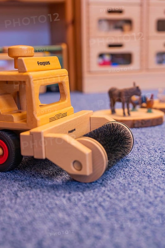 A wooden toy sweeper stands on blue carpet, with small animal figures in the background, infant and toddler daycare center, Gechingen, Germany