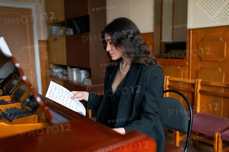 A focused musician reviews sheet music in a cozy practice room, sitting at a grand piano The warm tones of the room create an inviting and creative atmosphere