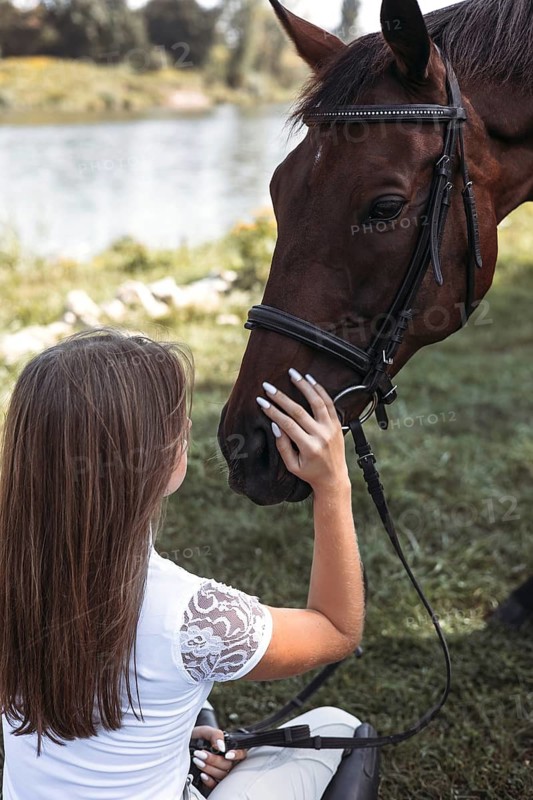 A young girl gently caresses a horse by a tranquil lakeside. The serene outdoor setting highlights the peaceful connection and mutual affection between them