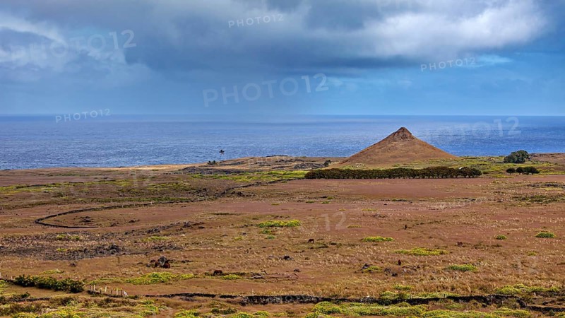 Lonely coastal landscape with a single hill under cloudy sky, The landscape of Easter Island in the Pacific Ocean