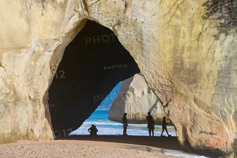 Natural rock formation with a view of the sea, people silhouetted in the cave on the sandy beach, Cathedral Cove, Hahei, Coromandel Peninsula, North Island, New Zealand