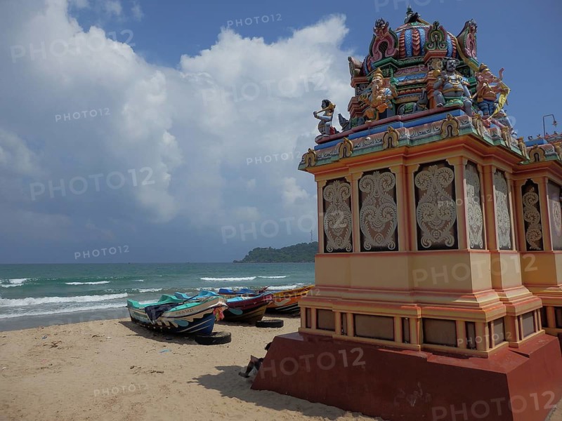 Several boats are moored on the beach next to an artfully designed Hindu temple, Thirukoneswaram Temple, with calm sea in the background, Trincomalee, Sri Lanka