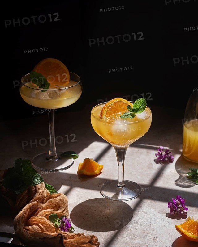 A stylish presentation of refreshing citrus cocktails garnished with orange slices and mint leaves, beautifully arranged on a table with vibrant flowers and soft lighting
