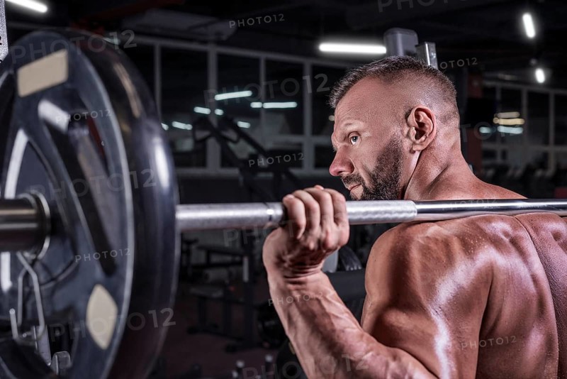 Image of a powerful athlete standing near a barbell rack in a gym. Fitness and bodybuilding concept.