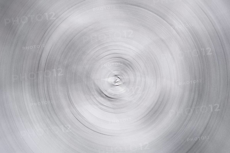 A distorted photograph showcasing an abstract spiral pattern in monochrome. The concentric circles create a sense of motion and depth, invoking a surreal, artistic feel