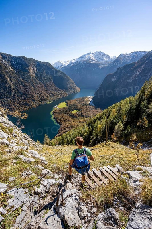 Mountaineers on a mountain hiking trail, Rinnkendlsteig, view of the Königssee, autumnal forest and yellow larches with snow-covered mountains, Berchtesgaden National Park, Berchtesgadener Land, Upper Bavaria, Bavaria, Germany