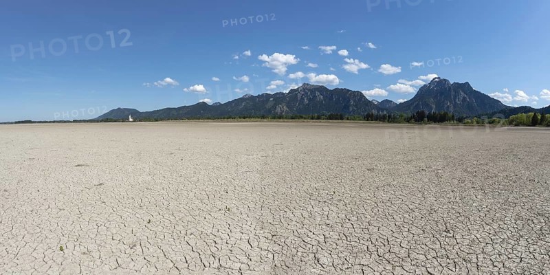 Cracked, dried out ground, waterless Forggensee in spring, behind it Tegelberg massif and Säuling, Ammergau Alps, near Füssen, Ostallgäu, Bavaria, Germany