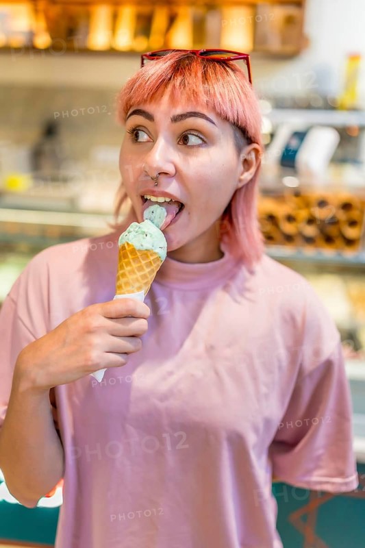 Vertical close-up portrait of a modern girl in pink hair eating ice cream in store