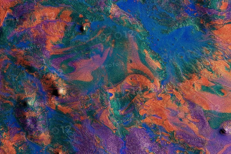 Vibrant metallic paints blend together in a chaotic yet mesmerizing pattern on this abstract background. The image captures a vivid display of blue, orange, and purple hues intermingling with shiny metallic effects