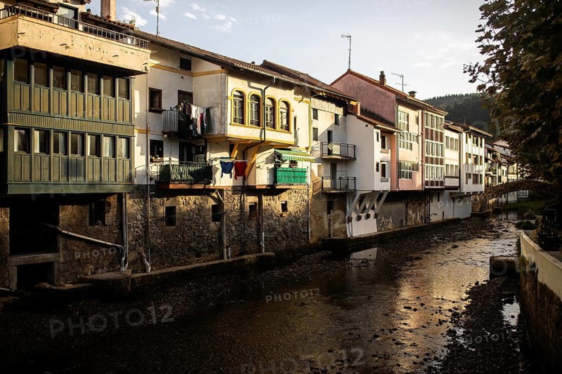 Evening sunlight bathes traditional Basque houses lining the river in Ea, Spain, highlighting their colorful facades and rustic charm A picturesque village scene