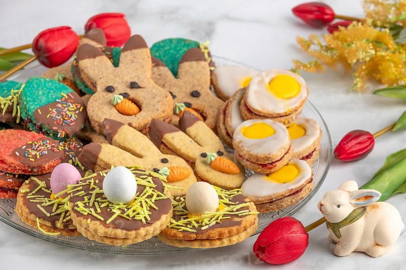 Plate of colourful Easter biscuits, decorated with carrots and eggs, next to red tulips