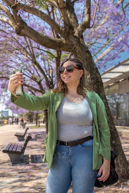 Smiling businesswoman taking a selfie in a park with blooming jacaranda mimosifolia trees