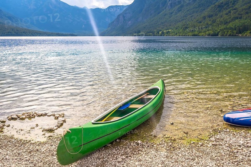 Green canoe with paddles rests on the pebbled shore of lake bohinj in slovenia, inviting visitors to explore the stunning alpine scenery during summer