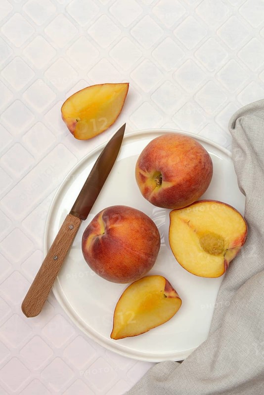 Cut peaches with knife on plate (Prunus persica)