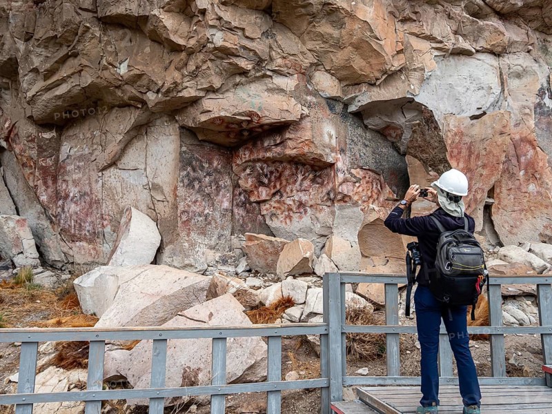 Tourist taking pictures, colored hands at the wall of the canyon, Cueva de las Manos, prehistoric paintings, Unesco world heritage, Argentina