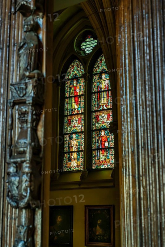 A view through a carved wooden pillar onto a luminous stained glass window in a church