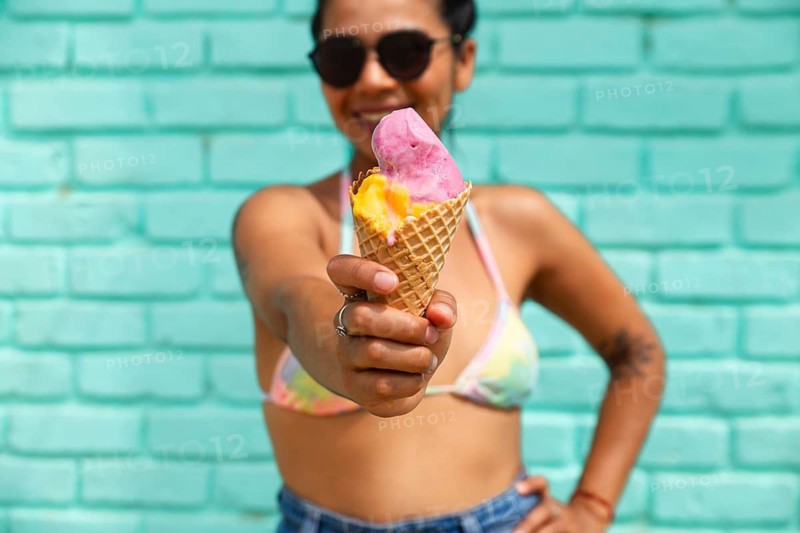A young Latin woman joyfully holds an ice cream cone against a turquoise background in Mancora, Peru. The scene captures a vibrant, sunny beach atmosphere