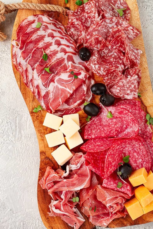 Assorted, sliced meat appetizer, prosciutto, salami and ham, with cheese and olives, on a wooden board, breakfast, top view, close-up, no people