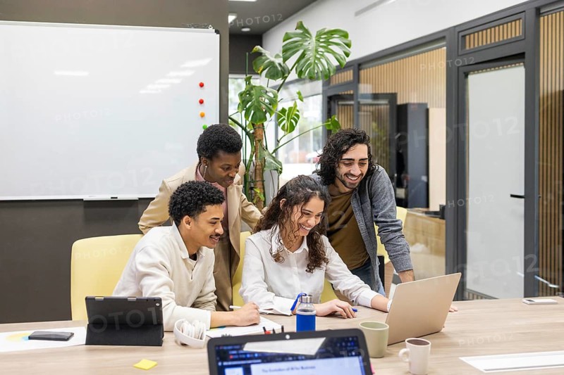Team of professionals collaborating in a modern office, engaged in a positive and productive discussion around a laptop, showcasing teamwork and creativity
