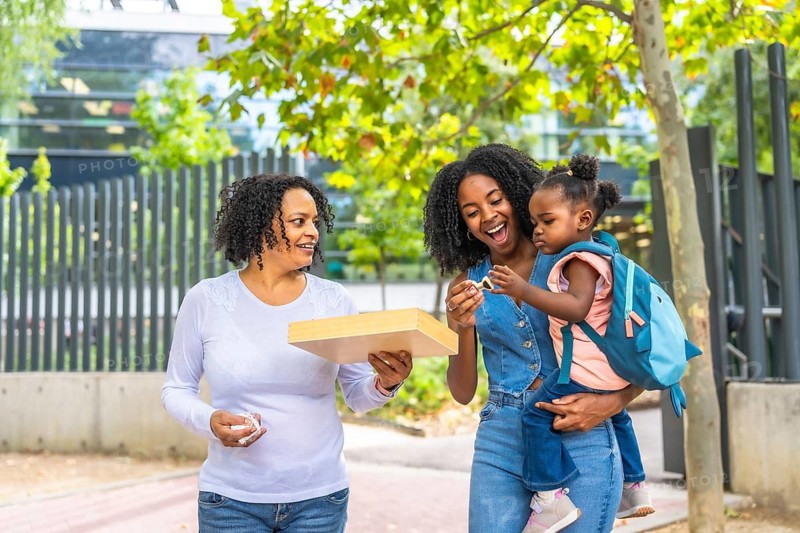 Three generation african female family in a public park carrying a girl and toys